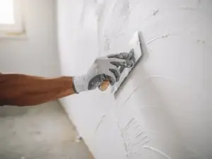 Gehandschoende hand die witte stuclaag glad strijkt op nieuwbouwmuur, fijne pleisterstructuur zichtbaar in close-up.