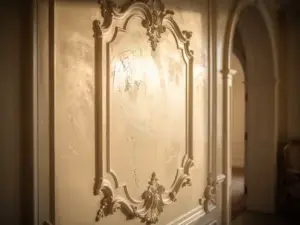 Sierlijk stucwerk paneel met Venetiaanse pleister in crème- en ivoortinten, verlicht door zijdelings invallend licht in een statig interieur.