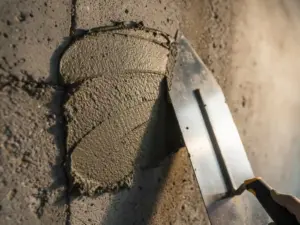 Verse cementreparatiemortel op ruwe betonwand met stalen spatel, natte oppervlaktextuur glanzend in warm zijlicht.