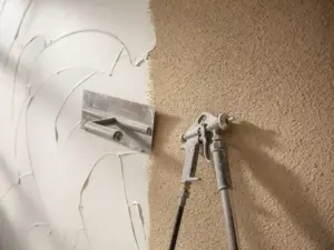 Pleistertroffel op glad handgepleisterde muur naast spuitpistool met fijn gespoten textuurafwerking, warme witte en zandbeige tinten.