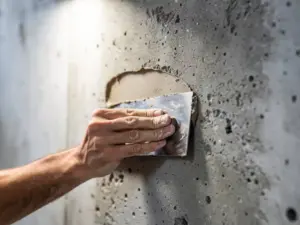 Stukadoor vult holte in ruwe betonwand met reparatiemortel, troffel strak tegen het grijze oppervlak gedrukt.